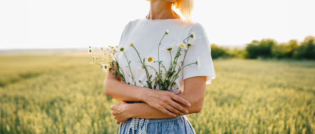 A woman holds flowers in a field and enjoys the natural beauty of the surroundings.