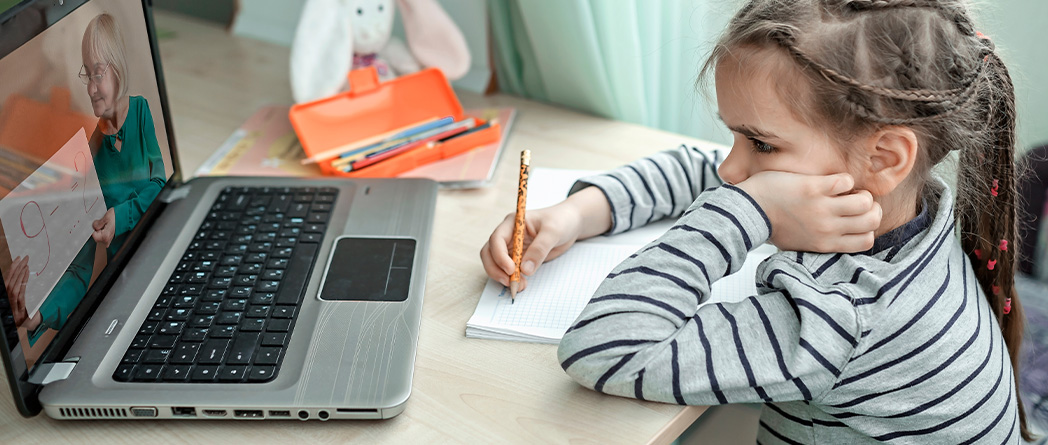 A young girl at a desk using a laptop, representing the balance of screen time and media in children's lives today.