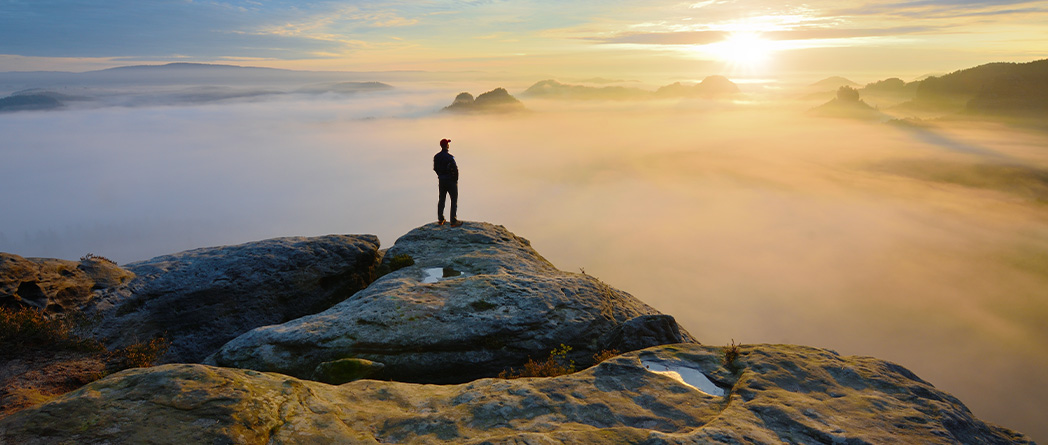 Person standing on mountaintop overlooking a sunrise through misty valleys