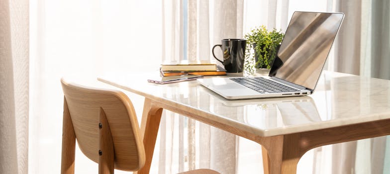 Minimalist workspace with natural light, a laptop, books, and coffee cup on desk