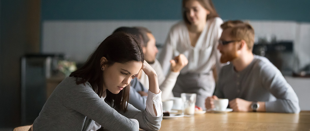 Person sitting quietly in a group, feeling out of place despite others engaging confidently